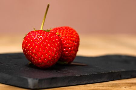 Close up of two strawberries on small black cutting board isolated outdoor on wooden table.の写真素材