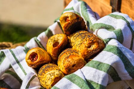 Sausages baked in dough sprinkled with salt and poppy seeds in a rustic basket. Sausages rolls, delicious homemade pastries in a rustic composition.の写真素材