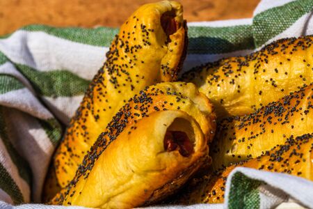 Sausages baked in dough sprinkled with salt and poppy seeds in a rustic composition. Sausages rolls, delicious homemade pastries.の写真素材