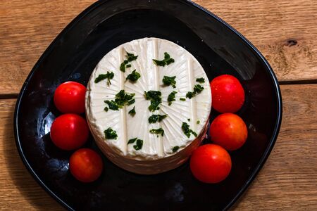 Breakfast food, cheese and cherry tomatoes on dish, on a rustic wooden plank board table background.の写真素材