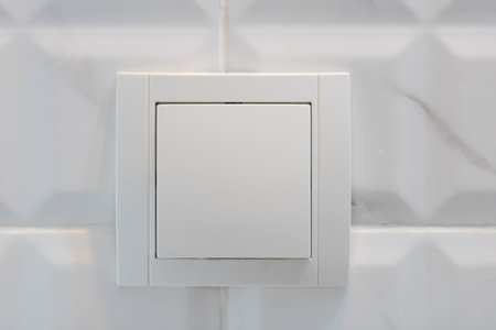 Close up view of white electric light switch on white tile. Building construction elements concept,...