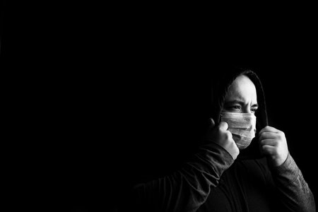 BW photo of sick young man with medical protective face mask illustrates pandemic coronavirus, Covid...