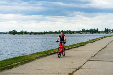 Young woman riding a bike, relaxing and have fun on the alleys of a park near a lake. Bucharest, Romania, 2020のeditorial素材
