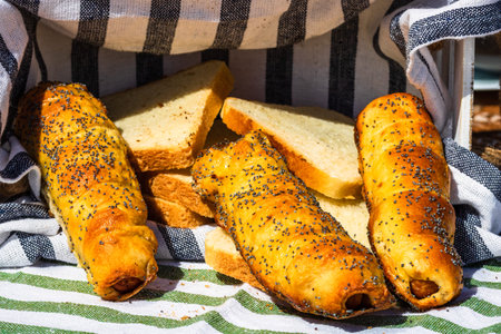 Sausages baked in dough sprinkled with salt and poppy seeds in a rustic composition. Sausages rolls,...