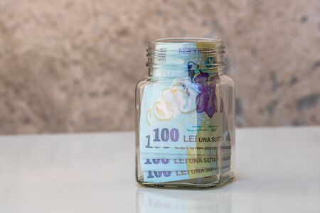 Composition with saving money romanian LEI banknotes in a glass jar. Concept of investing and keeping money, close up isolated.の写真素材