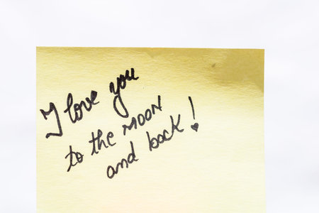 I love you to the moon and back handwriting text close up isolated on yellow paper with copy space.