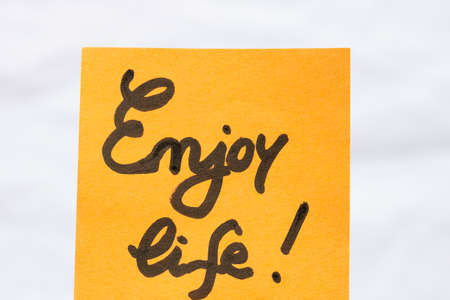Enjoy life handwriting text close up isolated on orange paper with copy space.の写真素材