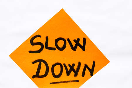 Slow down handwriting text close up isolated on yellow paper with copy space.の写真素材