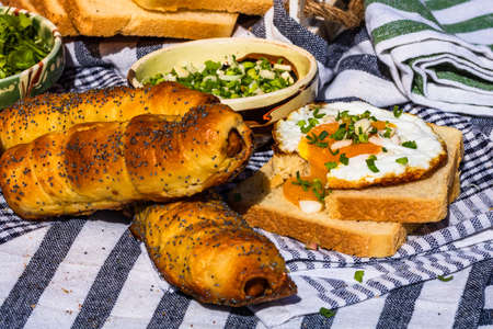 Rustic composition with sausages rolls, fried egg on toast bread, different bowls with sauce and chopped vegetables.の写真素材