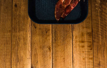 Pork chops with condiments and smoked sausage on a black frying pan, over wooden table, meat for bbq, top view, copy space, barbeque conceptの写真素材