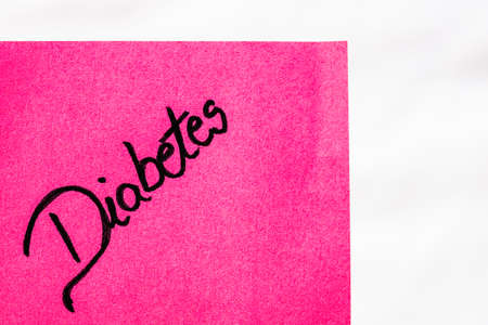 Diabetes handwriting text close up isolated on pink paper with copy space. Writing text on memo post reminderの写真素材