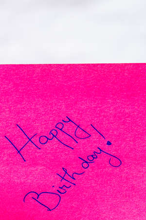 Happy birthday handwriting text close up isolated on pink paper with copy space. Writing text on memo post reminderの写真素材