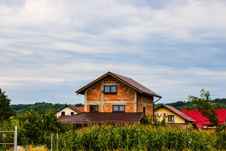 Development area at the edge of the village, facade of new unfinished house. Green corn field in...