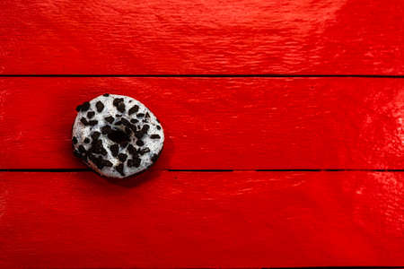 Colorful donuts on red wooden table. Sweet icing sugar food with glazed sprinkles, doughnut with chocolate frosting. Top view with copy spaceの写真素材