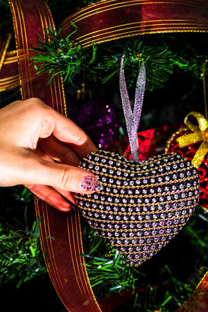 Hand putting heart shaped Christmas decorations on fir branches decorating Christmas tree, Christmas...