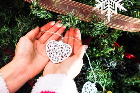 Hands holding Christmas ornament in front of Christmas tree. Decorating fir branches with Christmas...