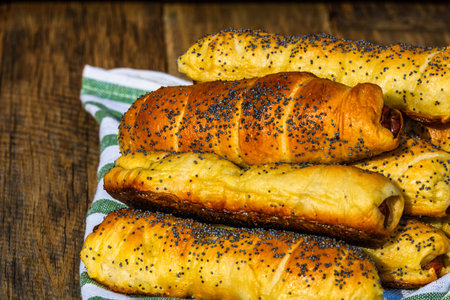 Sausages baked in dough sprinkled with salt and poppy seeds in a rustic composition. Sausages rolls,...