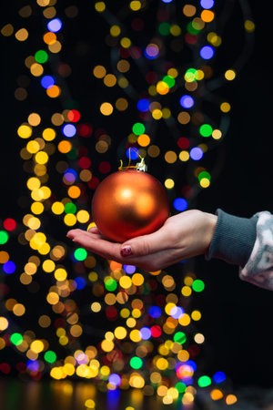 Woman's hands hold christmas decoration. Christmas and New Year holidays background, winter season with Christmas ornaments and blurred lightsの写真素材