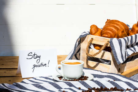 Coffee cup and buttered fresh French croissant on wooden crate. Food and breakfast concept. Morning message âstay positiveâ on white boardの写真素材