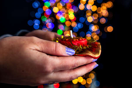 Holding Christmas decorated candle isolated on background with blurred lights. December season, Christmas composition.の写真素材