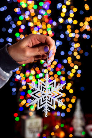 Holding Christmas snowflake decoration isolated on background with blurred lights. December season, Christmas composition.の写真素材