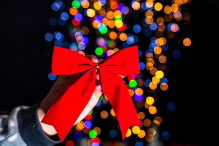 Holding Christmas red ribbon decoration isolated on background with blurred lights. December season, Christmas composition.の写真素材