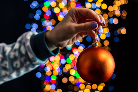 Holding Christmas bauble decoration isolated on background with blurred lights. December season, Christmas composition.の写真素材