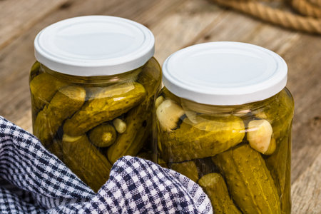 Glass jars with pickled red bell peppers and pickled cucumbers (pickles) isolated. Jars with variety of pickled vegetables. Preserved food concept in a rustic composition.の写真素材