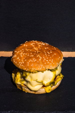 Homemade beef cheeseburger with melting cheese, tomatoes, onions, pickles isolated on a black stone plate.の写真素材