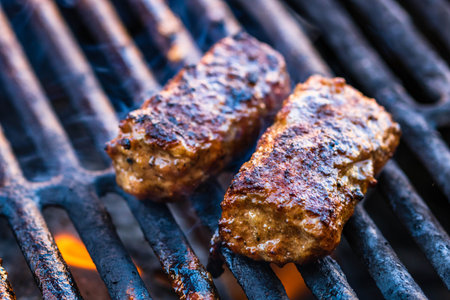 Preparing meat rolls called mici or mititei on barbecue. close up of grill with burning fire with flame and smoke.の写真素材