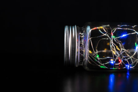 Colorful fairy lights in glass jar isolated on black background.の写真素材