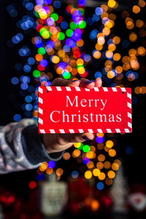 Holding Merry Christmas sign isolated on background with blurred lights. December season, Christmas composition.の写真素材