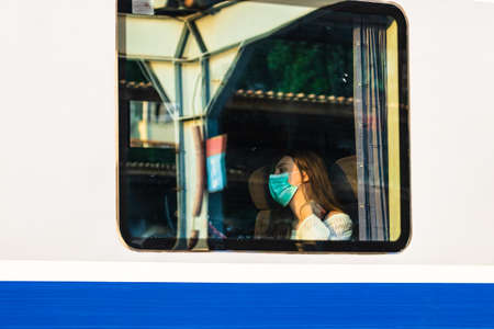 Young woman wearing surgical face mask protect against coronavirus infection at public train station, social distancing concept. Train at train platform in Bucharest, Romania, 2020のeditorial素材