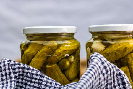 Glass jars with pickled red bell peppers and pickled cucumbers (pickles) isolated. Jars with variety of pickled vegetables. Preserved food concept in a rustic composition.の写真素材