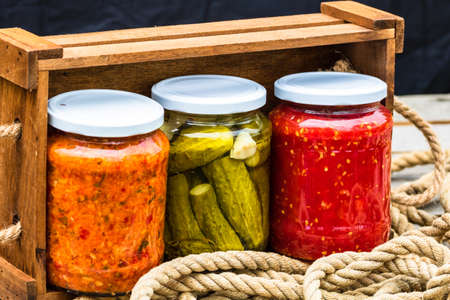 Wooden crate with glass jars with variety of canned vegetables isolated.の写真素材