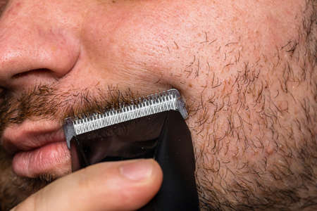 Man shaving or trimming his beard using a hair clipperの写真素材