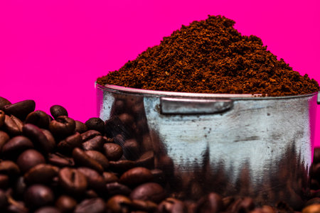 Coffee beans and portafilter with ground coffee in a composition on a pink background.