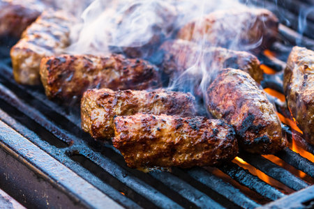Preparing meat rolls called mici or mititei on barbecue. close up of grill with burning fire with flame and smoke.の写真素材