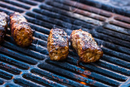Preparing meat rolls called mici or mititei on barbecue. close up of grill with burning fire with flame and smoke.の写真素材