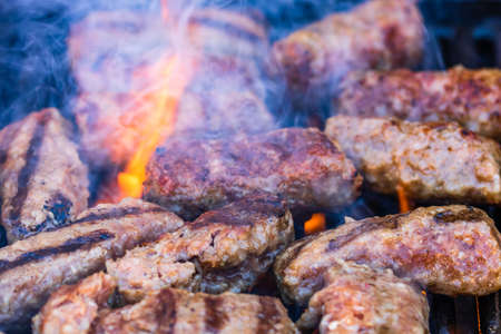 Preparing meat rolls called mici or mititei on barbecue. close up of grill with burning fire with flame and smoke.の写真素材