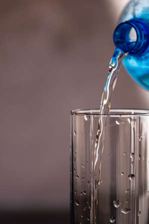 Pouring water from blue plastic bottle into a glass on blurred background. Selective focus, shallow DOF and copy spaceの写真素材