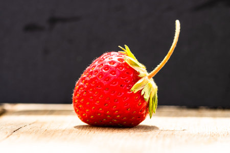Close up of one strawberry on wooden board isolated on black background