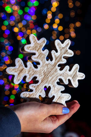Holding Christmas snowflake decoration isolated on background with blurred lights. December season, Christmas composition.の写真素材