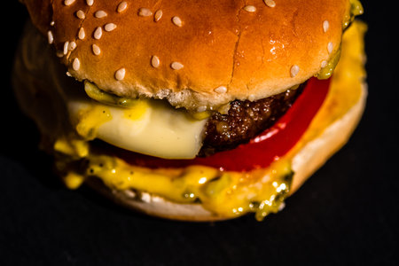 Detail of beef cheeseburger with melted cheese isolated on black background.