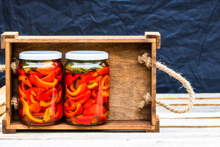 Wooden crate with glass jars with pickled red bell peppers.Preserved food concept, canned vegetables isolated in a rustic composition.の写真素材