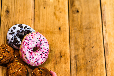 Colorful donuts on wooden table. Sweet icing sugar food with glazed sprinkles, doughnut with chocolate frosting. Top view with copy spaceの写真素材