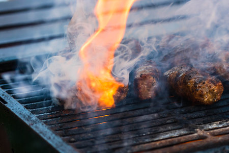 Preparing meat rolls called mici or mititei on barbecue. close up of grill with burning fire with...