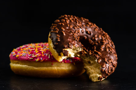 Fresh tasty colored donuts with sprinkles on black background
