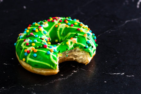 Green glazed donut with sprinkles isolated. Close up of colorful bitten donut.
