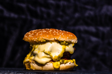 Detail of fresh tasty beef cheeseburger with melted cheese isolated on black backgroundの写真素材